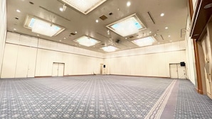 Un salón de conferencias amplio y vacío, con alfombra estampada, iluminación empotrada y un techo alto.