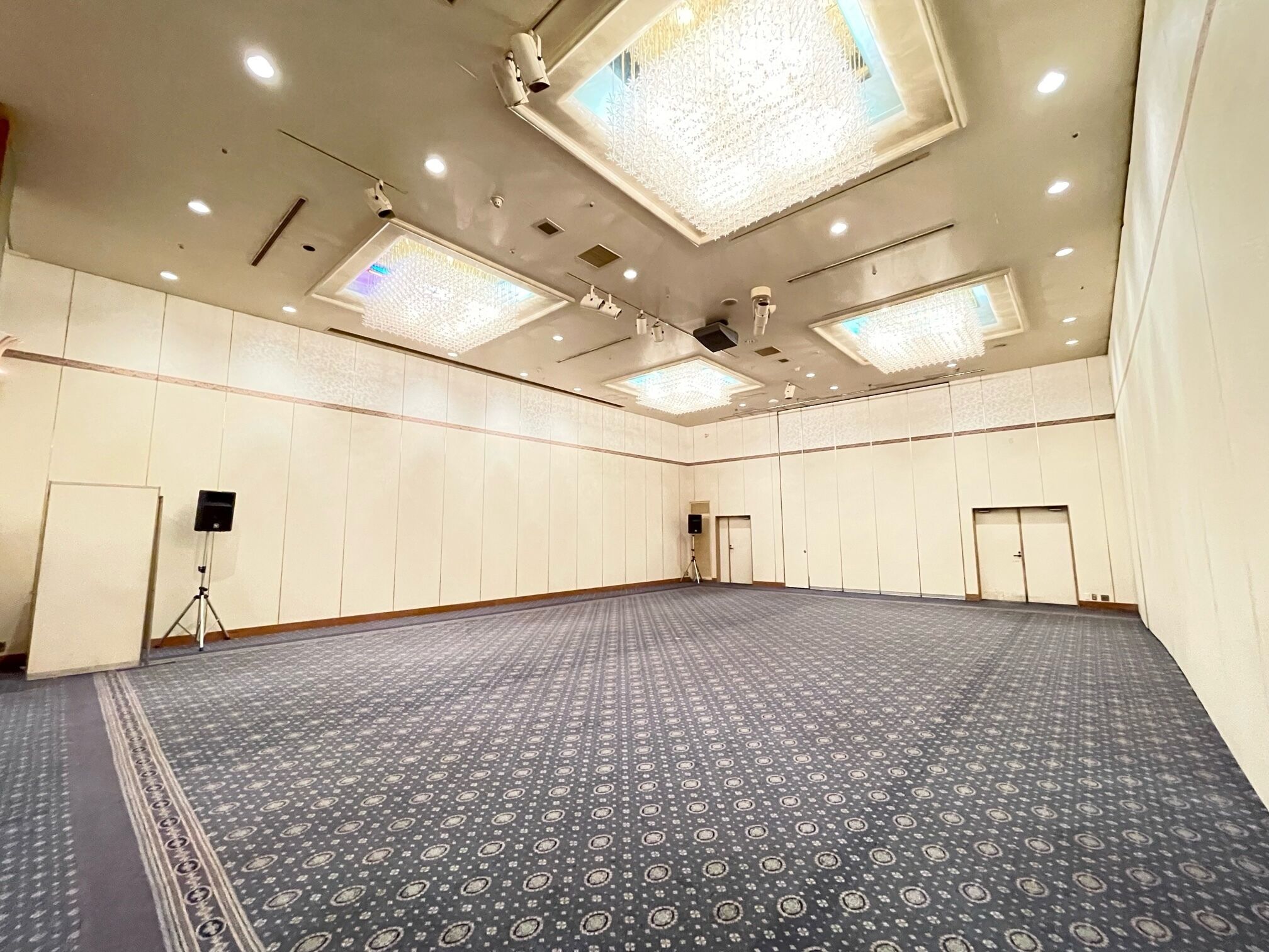 A large, empty conference room with a patterned carpet, recessed ceiling lights, and a chandelier.