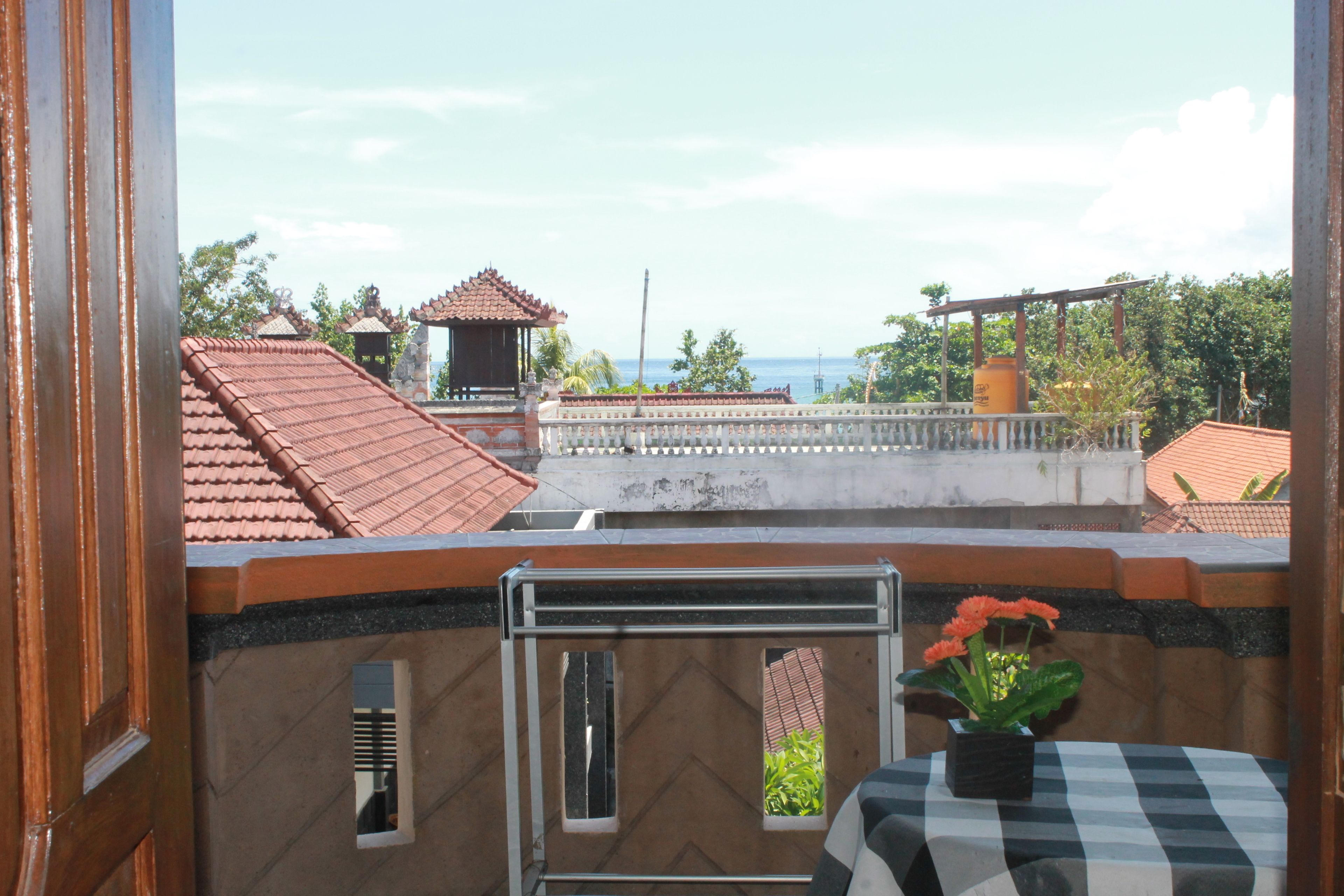 A balcony with a view of the sea, a tiled roof, and a small table with a potted plant.