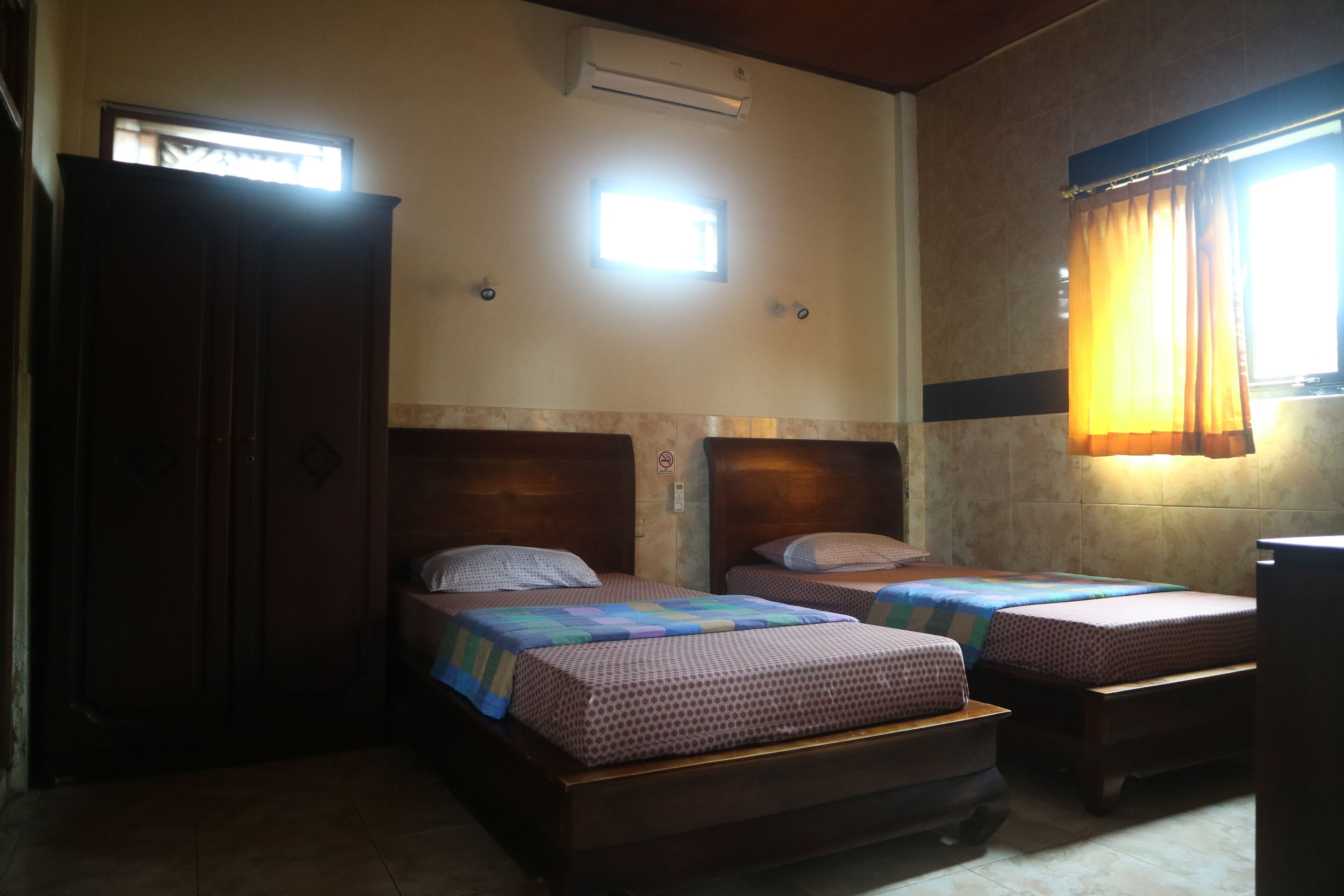 A small, dimly lit room with two wooden beds, a wooden wardrobe, and a window with curtains.