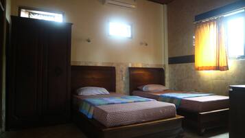 A small, dimly lit room with two wooden beds, a wooden wardrobe, and a window with curtains.