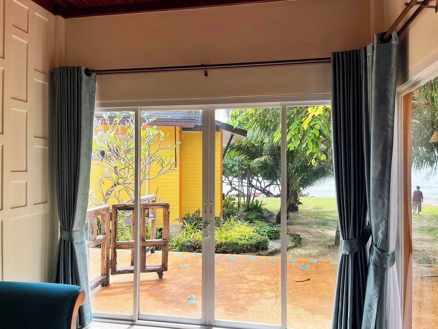 A room with a sliding glass door leading to an outdoor area with a yellow wall, a wooden table, and a chair.