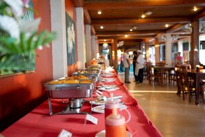 A buffet setup with multiple food stations and a long table covered with a red tablecloth.