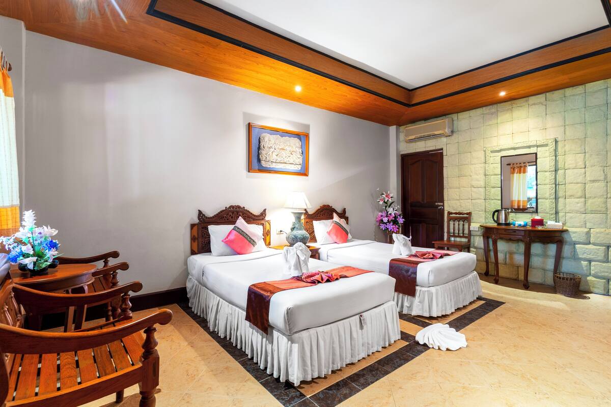 A hotel room with two beds, wooden furniture, a painting on the wall, and a stone wall.