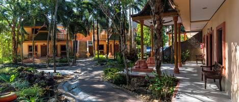 A tropical resort courtyard with a curved pathway, palm trees, and traditional architecture.