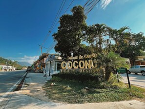 A sign for Coconu Beach Resort with a tropical garden in the foreground.