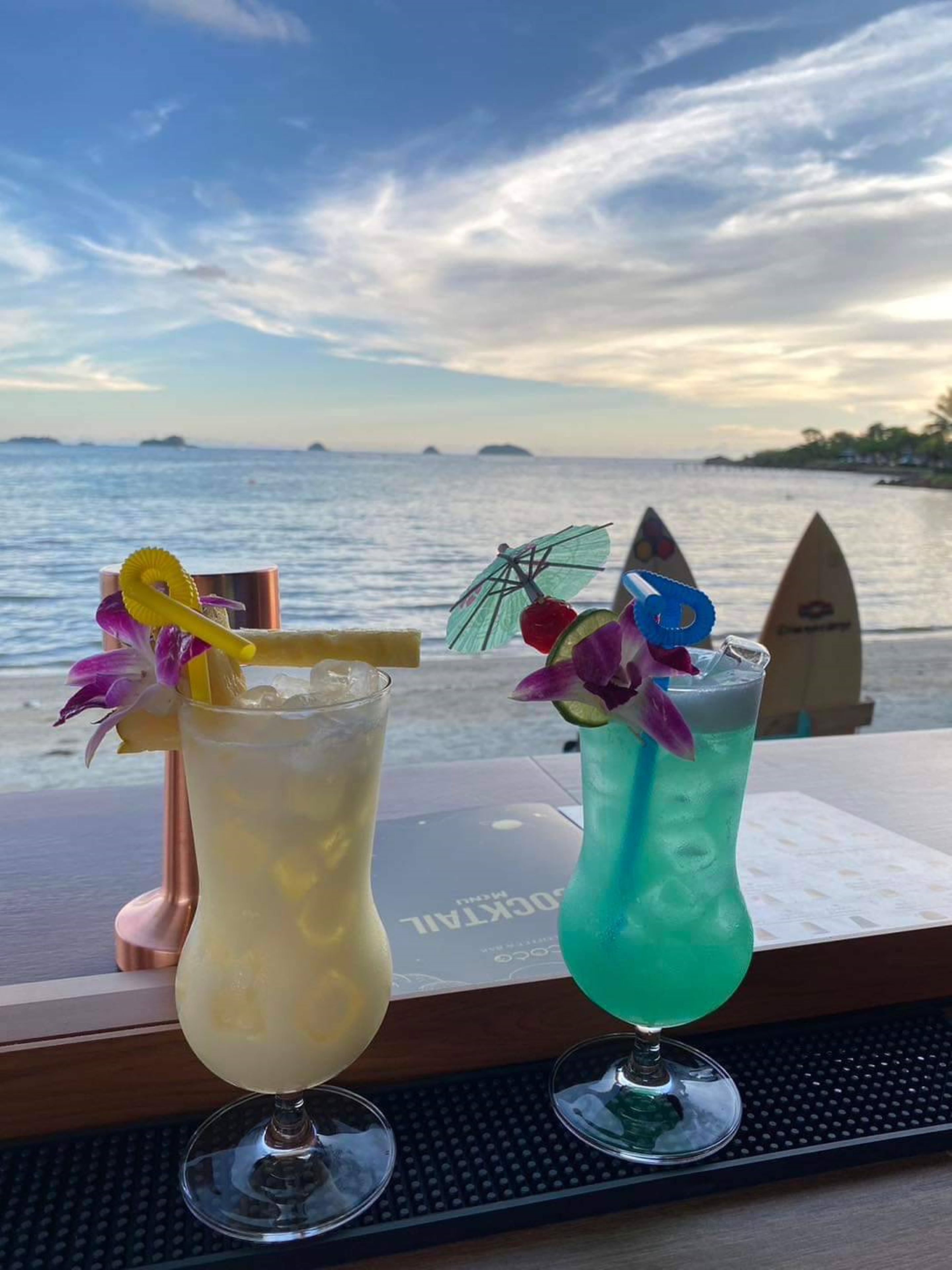 Zwei Cocktails auf einer Bartheke mit Blick auf das Meer und Inseln im Hintergrund.