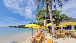 A beachside café with yellow umbrellas and wooden chairs, a signboard for 'Coco Coffee & Bar', and a palm tree. - Coconut Beach Resort (Ko Chang)