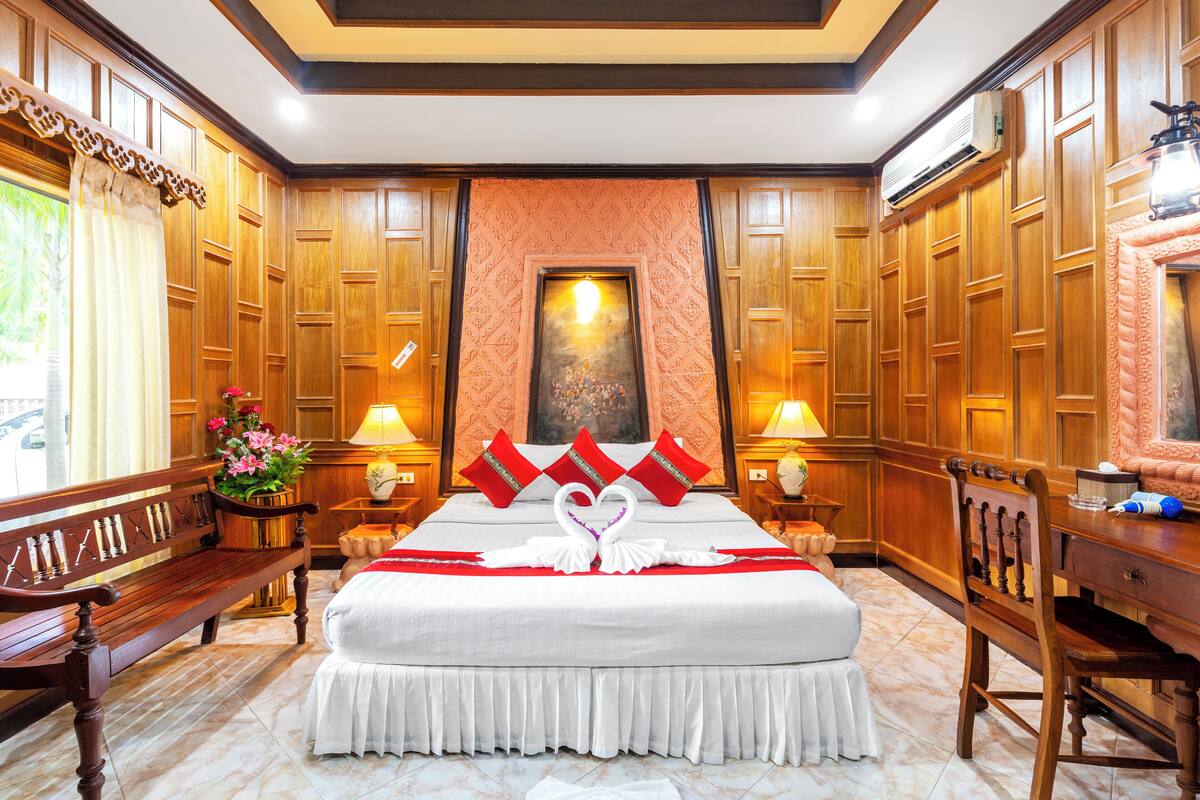 A hotel room with a large bed, wooden paneling, a bench, and a desk.