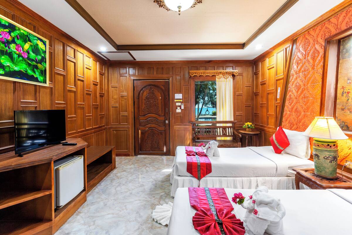 A hotel room with wooden paneling, two beds, a TV, a small table, and a lamp.