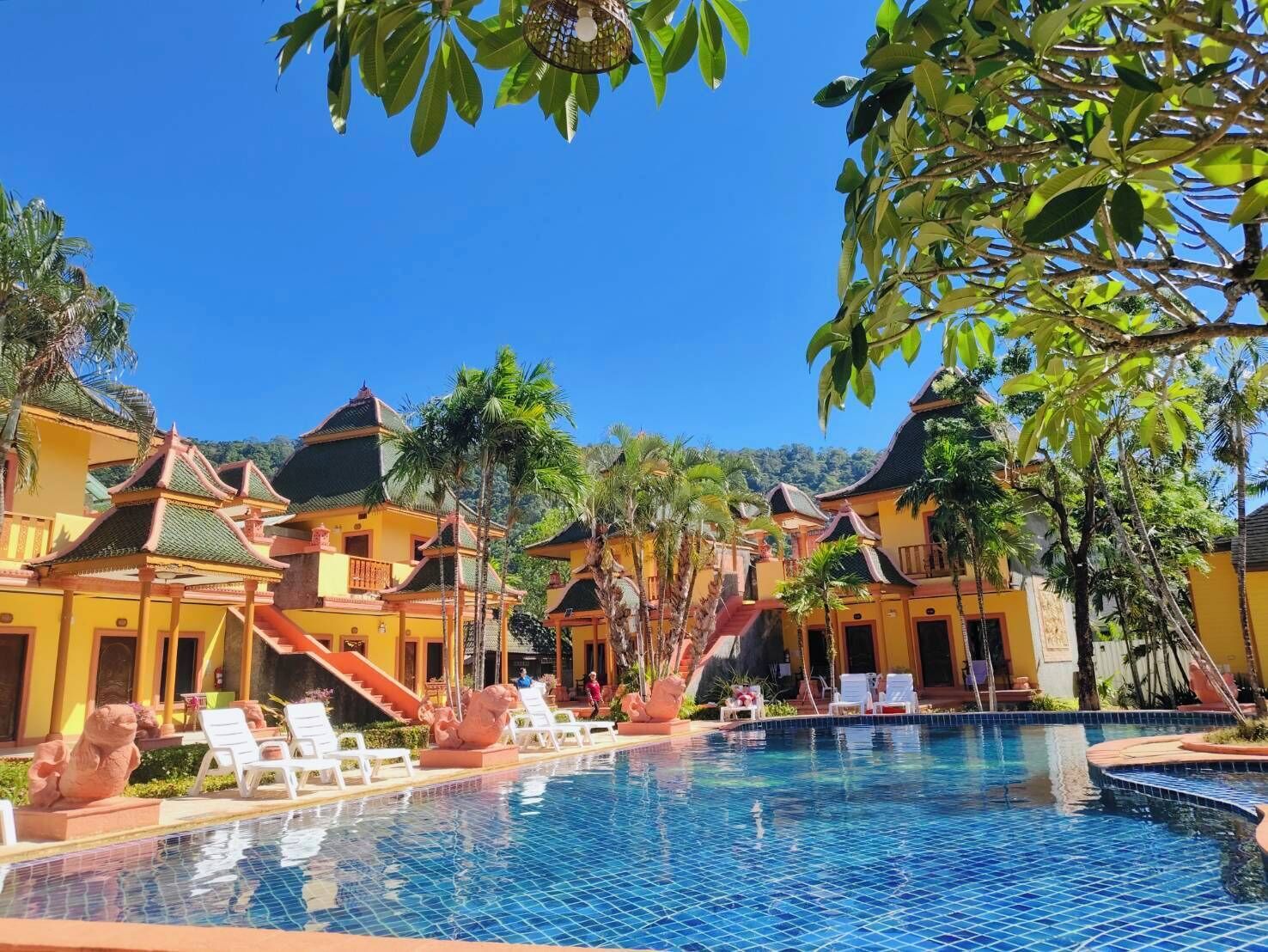 Um resort com piscina, arquitetura tradicional e palmeiras.