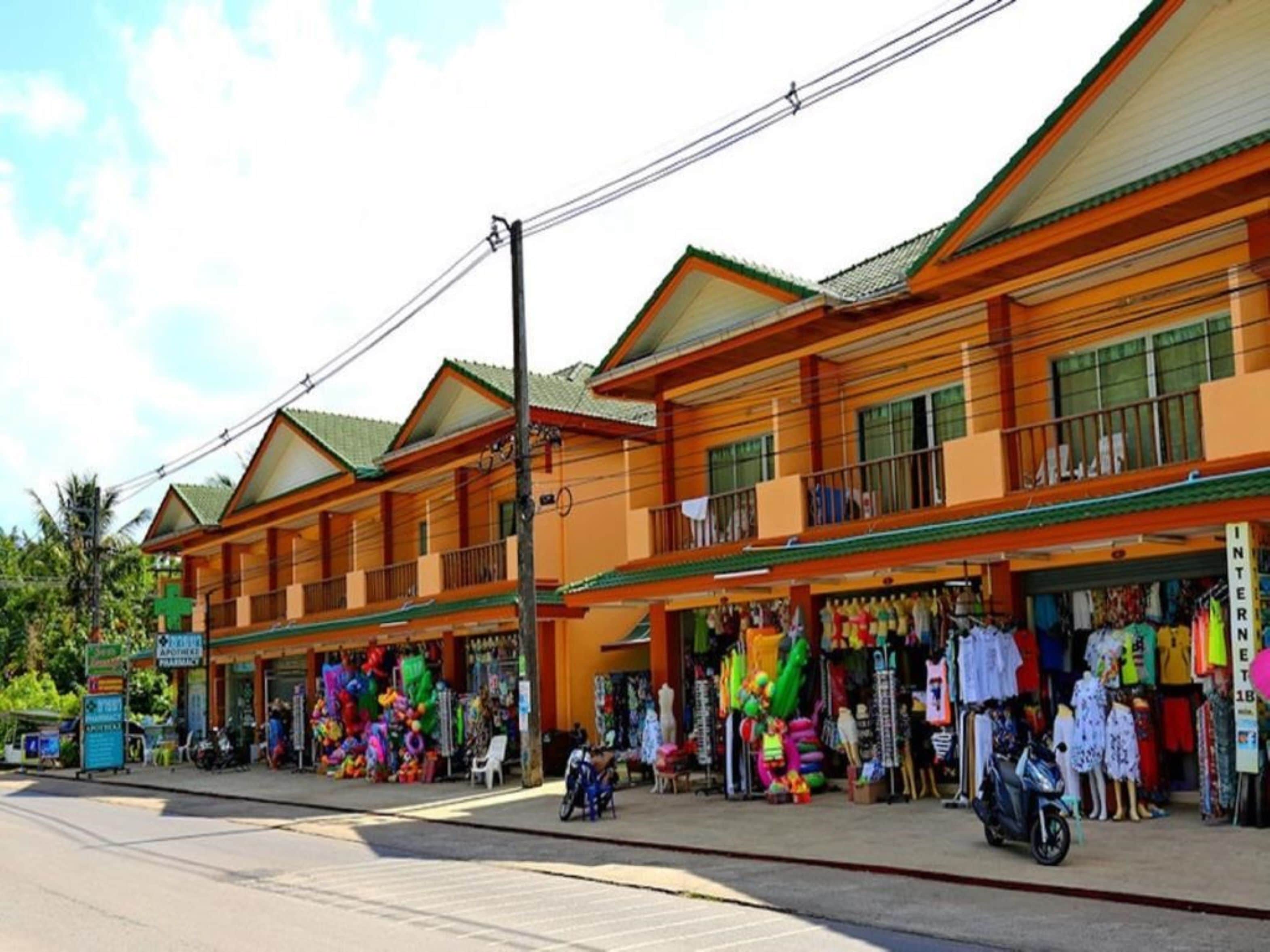 A row of shops with colorful items on display, a pharmacy, and a sign for an internet cafe.