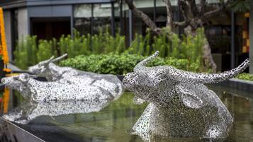 A sculpture of a bull and a cow in a reflective pool, with a modern building and greenery in the background.
