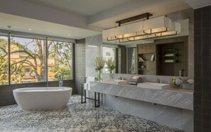 Un baño moderno con una bañera independiente, dos lavamanos, un espejo grande y vistas al exterior.