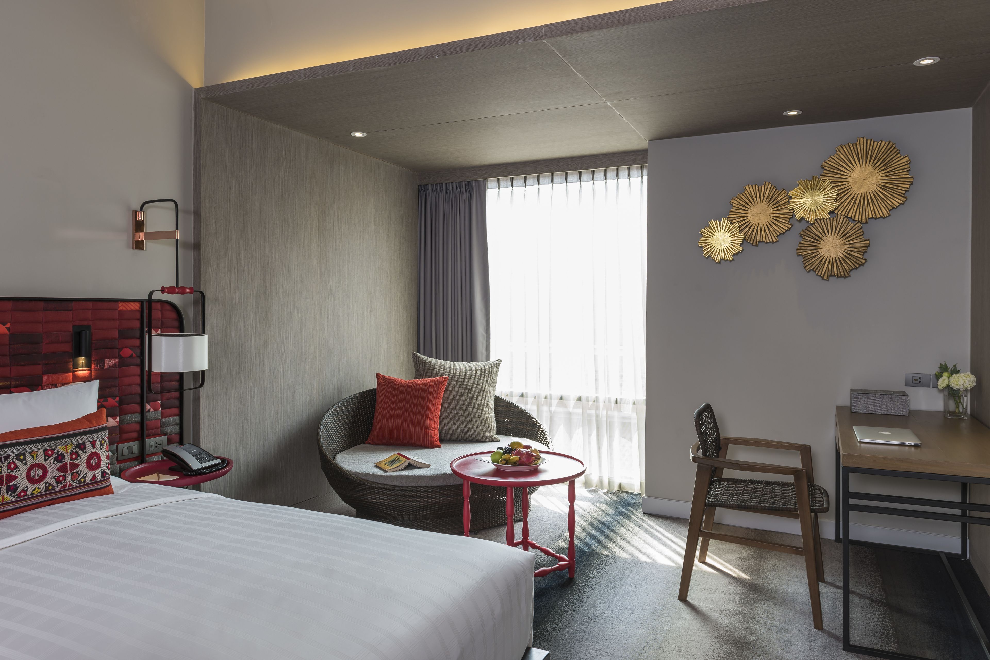 A hotel room with a bed, a seating area with a chair and a small table, a desk with a chair, and a large window with curtains.