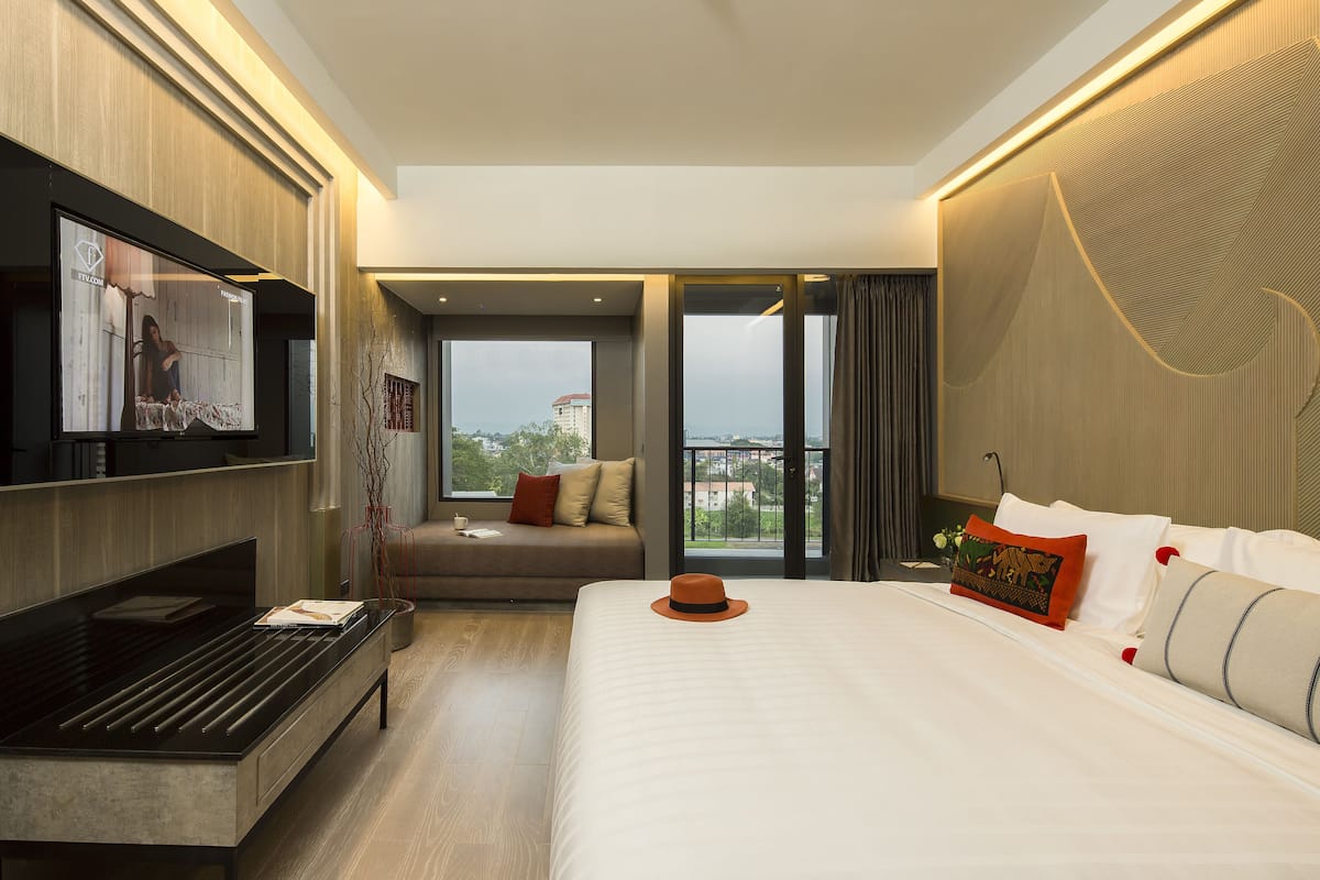 Quarto de hotel moderno com uma cama grande, televisão de tela plana na parede, sofá e varanda com vista para a cidade.