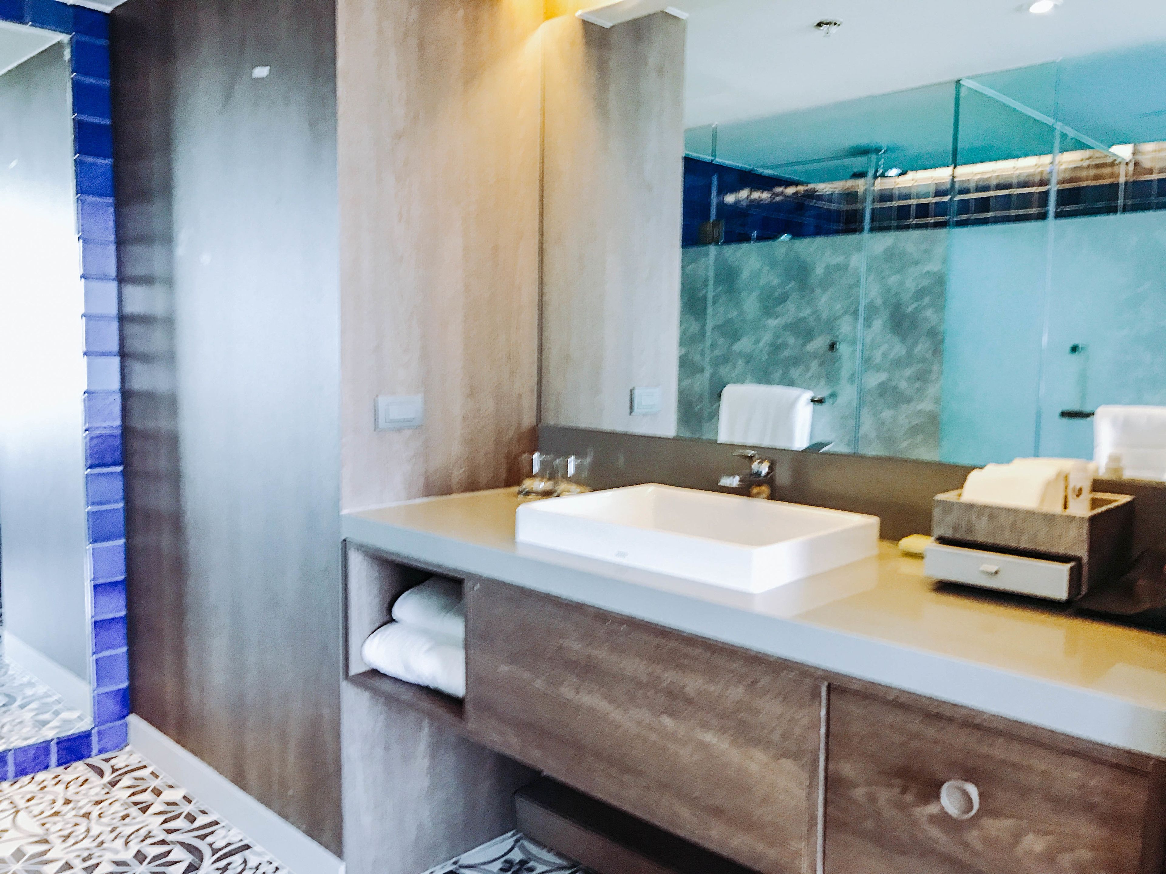 A modern bathroom with a large mirror, a white sink, and a vanity with a towel rack.