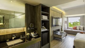 Habitación de hotel moderna con un espejo grande, televisión integrada, sofá junto a la ventana y una kitchenette compacta.