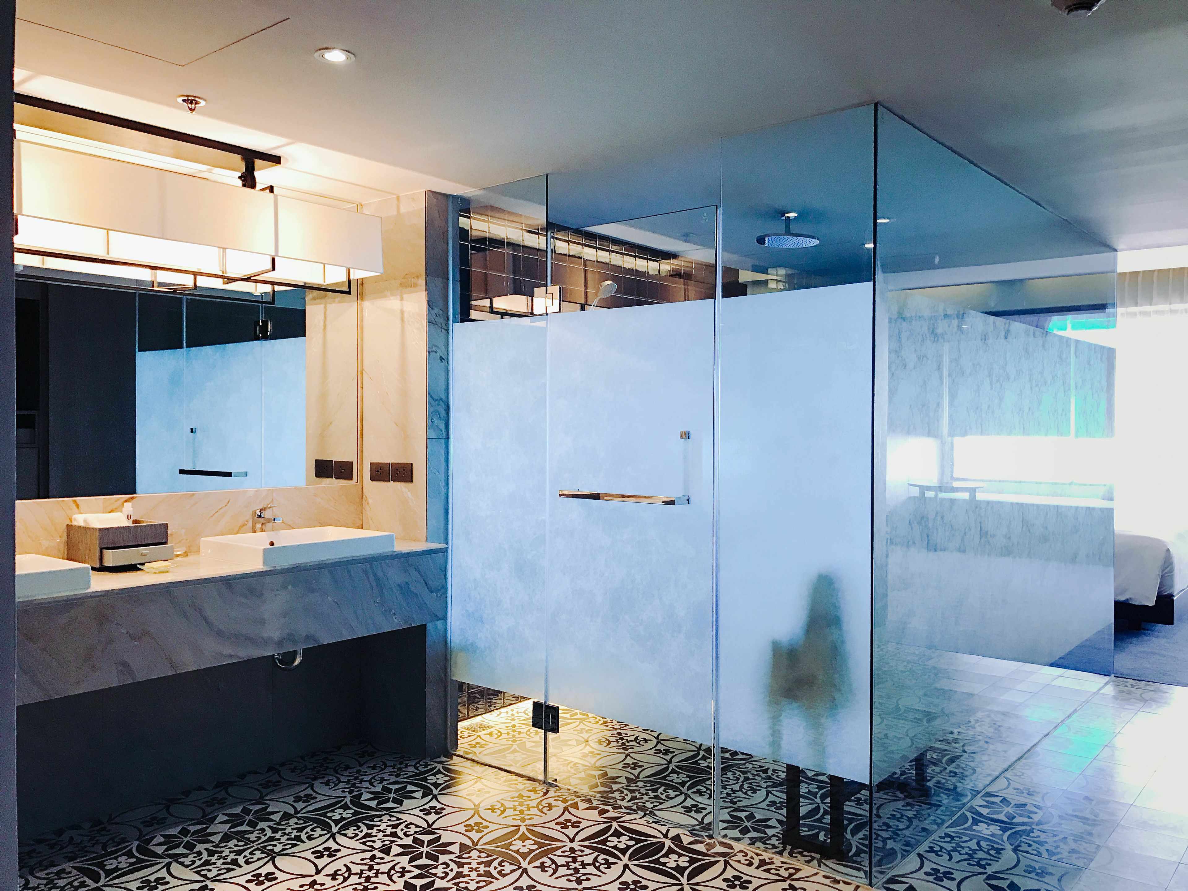 A modern bathroom with a glass-enclosed shower, a marble vanity, and patterned floor tiles.
