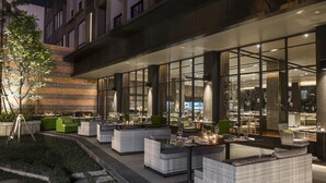 An outdoor dining area with modern furniture and large windows overlooking the street.