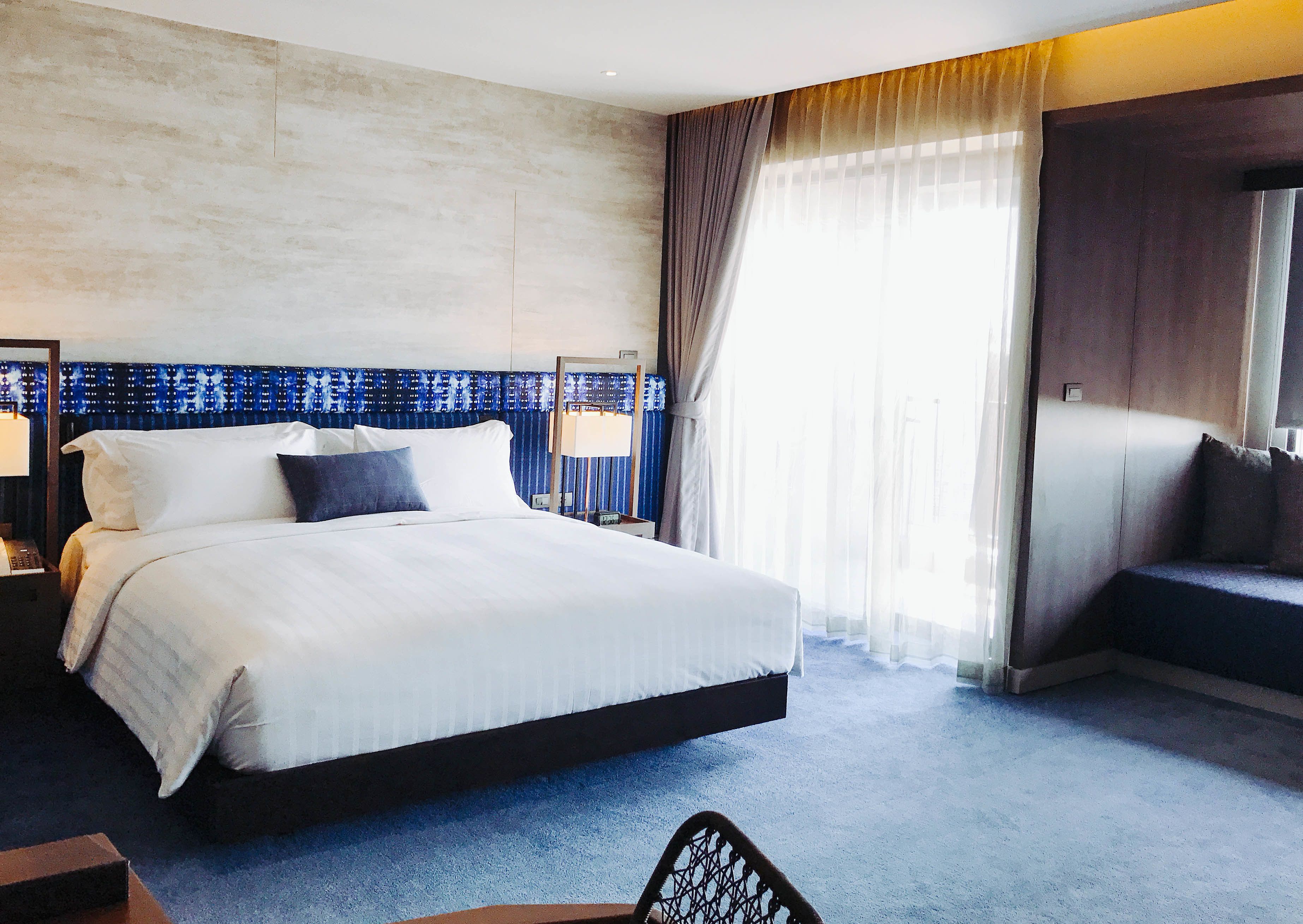 Habitación de hotel con una cama grande, un escritorio, una silla y un ventanal con cortinas.