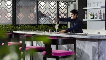 A bar area with a marble countertop, black bar stools with pink cushions, and a decorative wall with a geometric pattern.