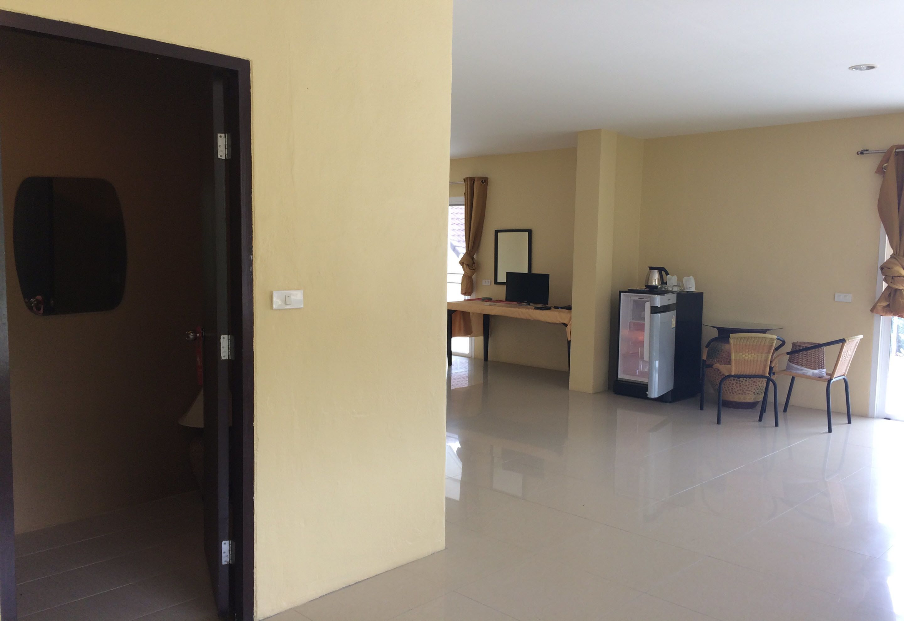 A hotel room with a desk, chair, and a refrigerator.