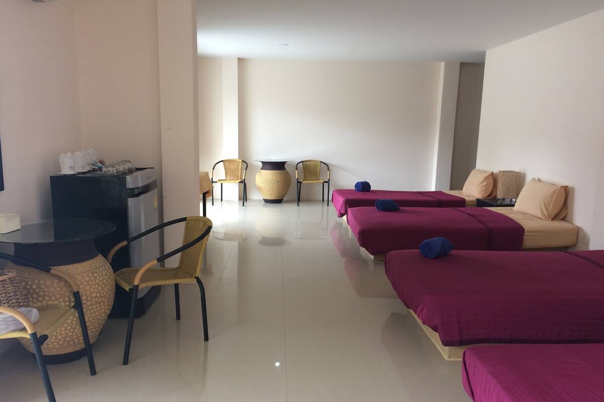 Hotellihuoneessa on lasipöytä, kaksi keltaista tuolia, punaisilla ja beigenvärisillä koristetyynyillä varustettu sohva sekä suuri maljakko.
