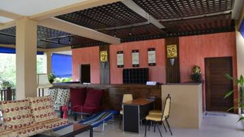 A hotel lobby with a reception desk, seating area with patterned sofas, a dining table, and a blue-striped chair.