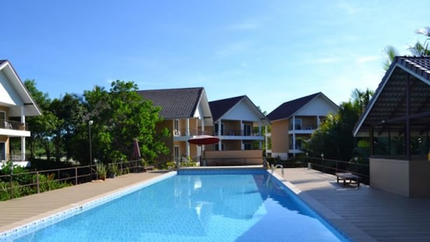 Ein rechteckiger Swimmingpool mit umlaufender Holzterrasse, vor einer Kulisse aus Wohnhäusern und Grünflächen.