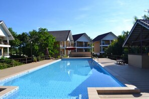 Una piscina rectangular con cubierta de madera, con edificios residenciales y vegetación de fondo.