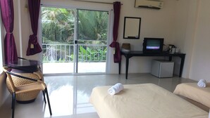 Ein Hotelzimmer mit Bett, Schreibtisch mit Computer, Stuhl und Blick auf Palmen durch die Glastür.