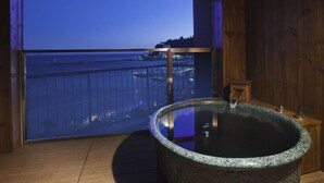 A spa area with a hot tub and a large window overlooking a cityscape at dusk. - Atami Seaside Spa & Resort (Atami)