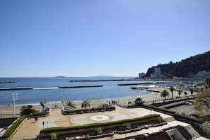 En strandpromenad med ett centralt, cirkelformat torg, en strand och en bakgrund av kullar och byggnader.