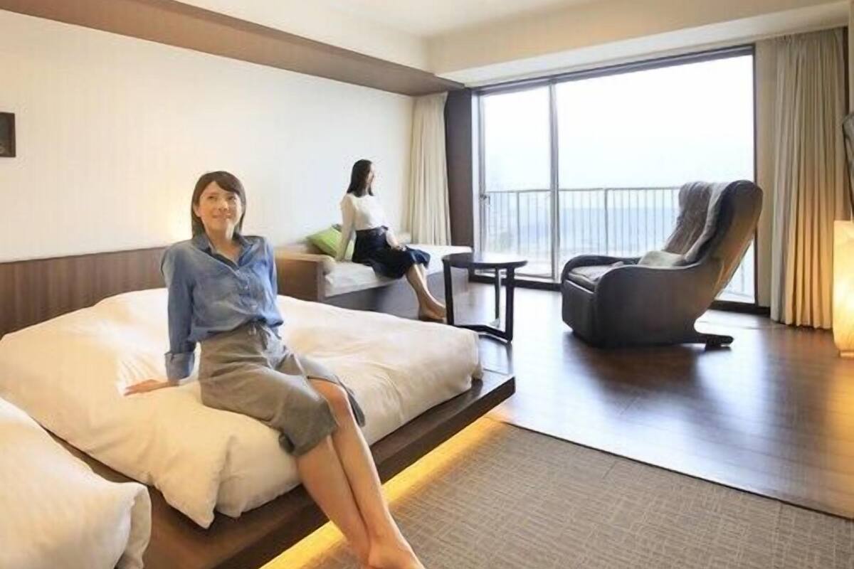 A hotel room with a large bed, a sofa, a chair, and a balcony with a view.