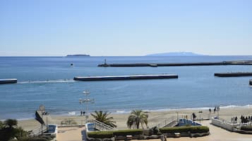 A coastal promenade with a beach, a pier, and a statue.