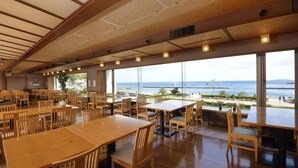 A spacious dining area with large windows offering a view of the sea. Tables and chairs are arranged neatly. - Atami Seaside Spa & Resort (Atami)