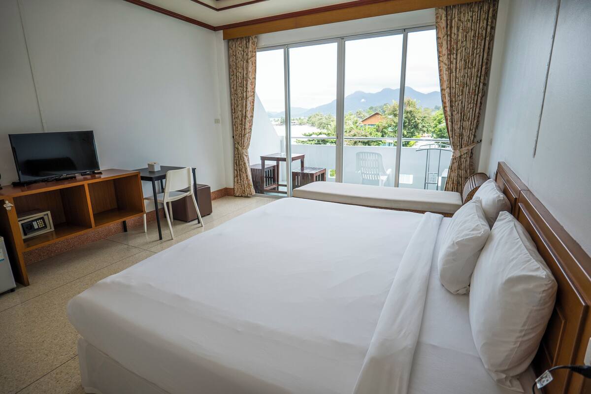 Habitación de hotel con una cama grande, televisión, escritorio y balcón con vistas a las montañas.