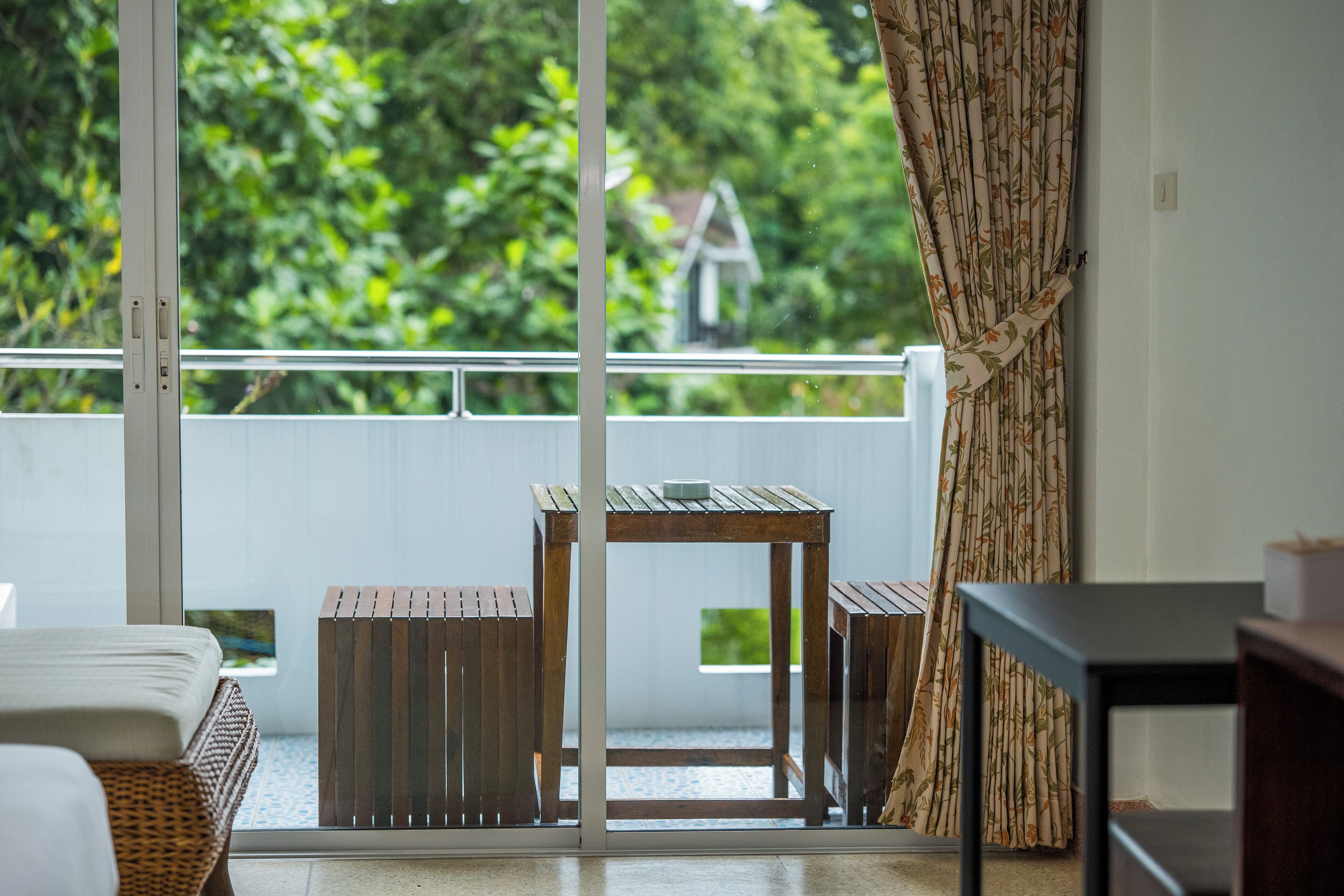 Varanda com mesa e cadeiras de madeira, um sofá de vime e vista para o verde e uma casa.