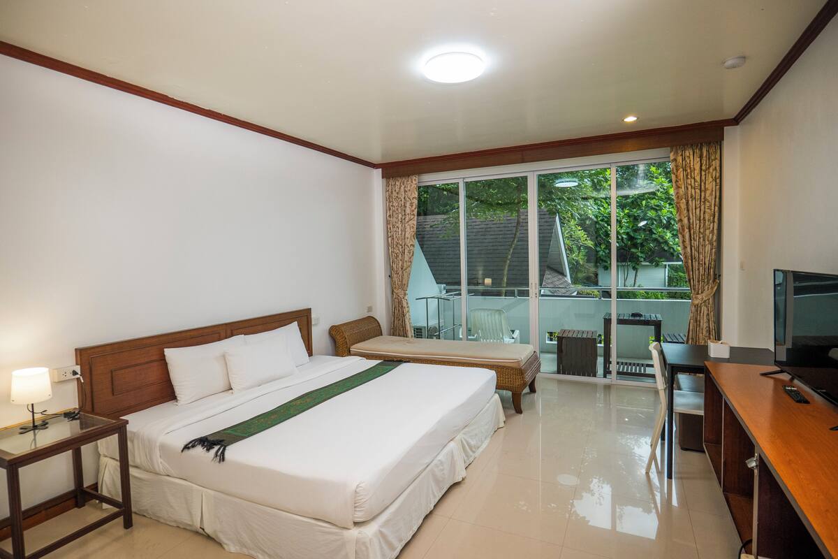 Habitación de hotel con una cama grande, un escritorio, un televisor y un balcón con vistas al exterior.