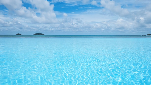 Mar azul transparente con aguas tranquilas e islas distantes bajo un cielo parcialmente nublado.
