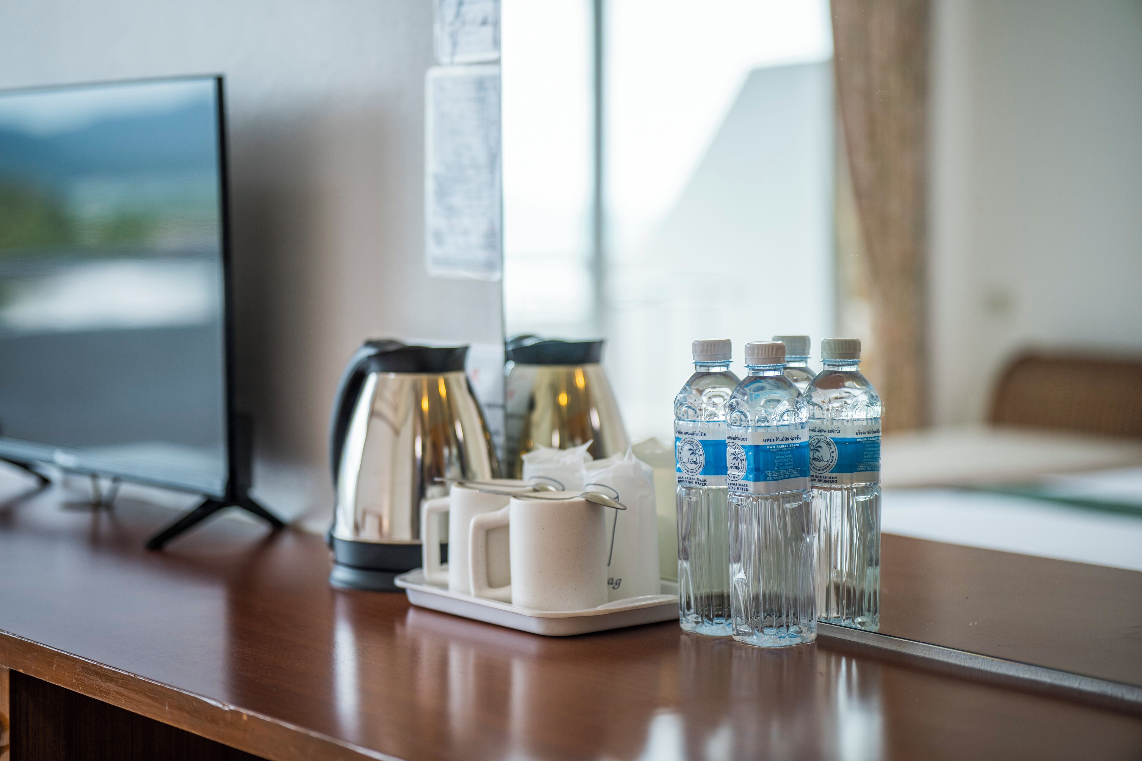 Una habitación de hotel con un escritorio de madera, una cafetera, una taza y varias botellas de agua.
