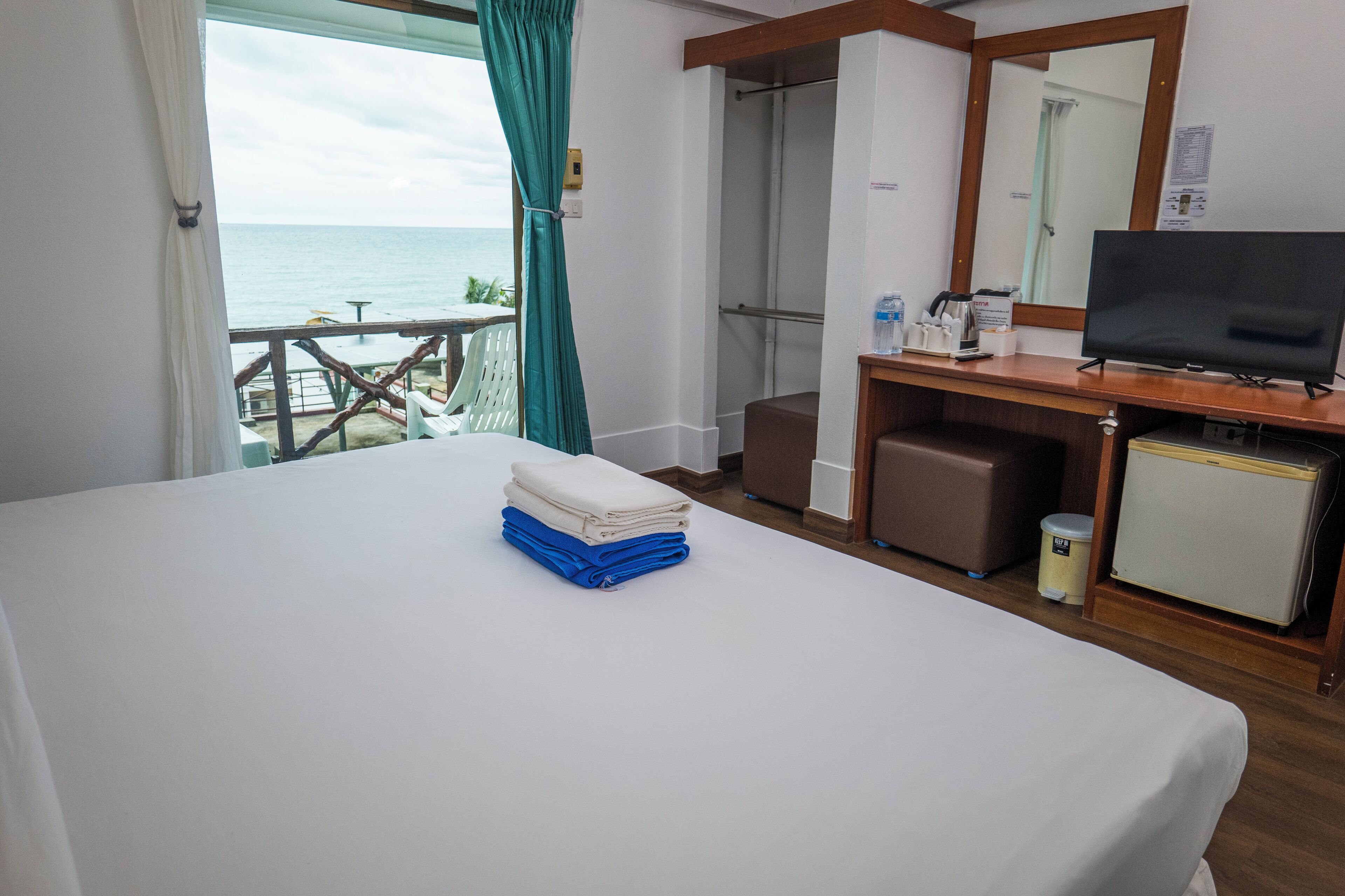 Een hotelkamer met een bed, een bureau met een televisie, een kleine koelkast en uitzicht op de oceaan.