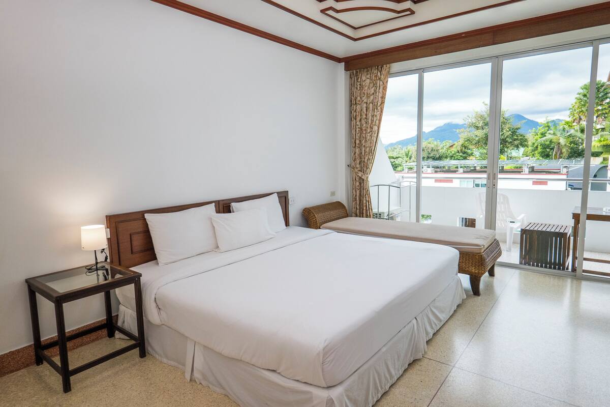Habitación de hotel con una cama grande, una mesita de noche, una silla y vistas al exterior.