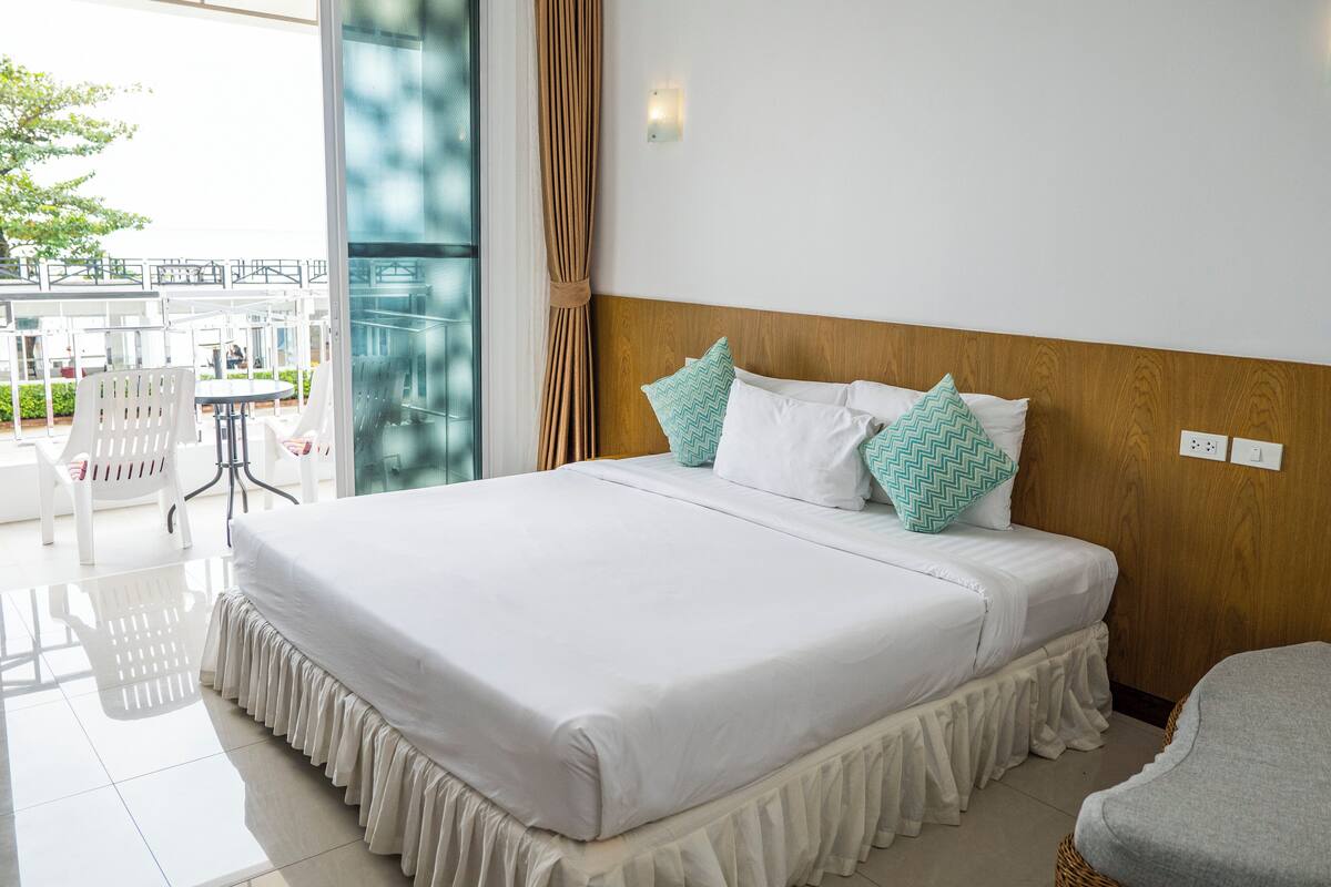 Habitación de hotel con una cama grande, cabecero de madera y vistas al área de estar al aire libre.