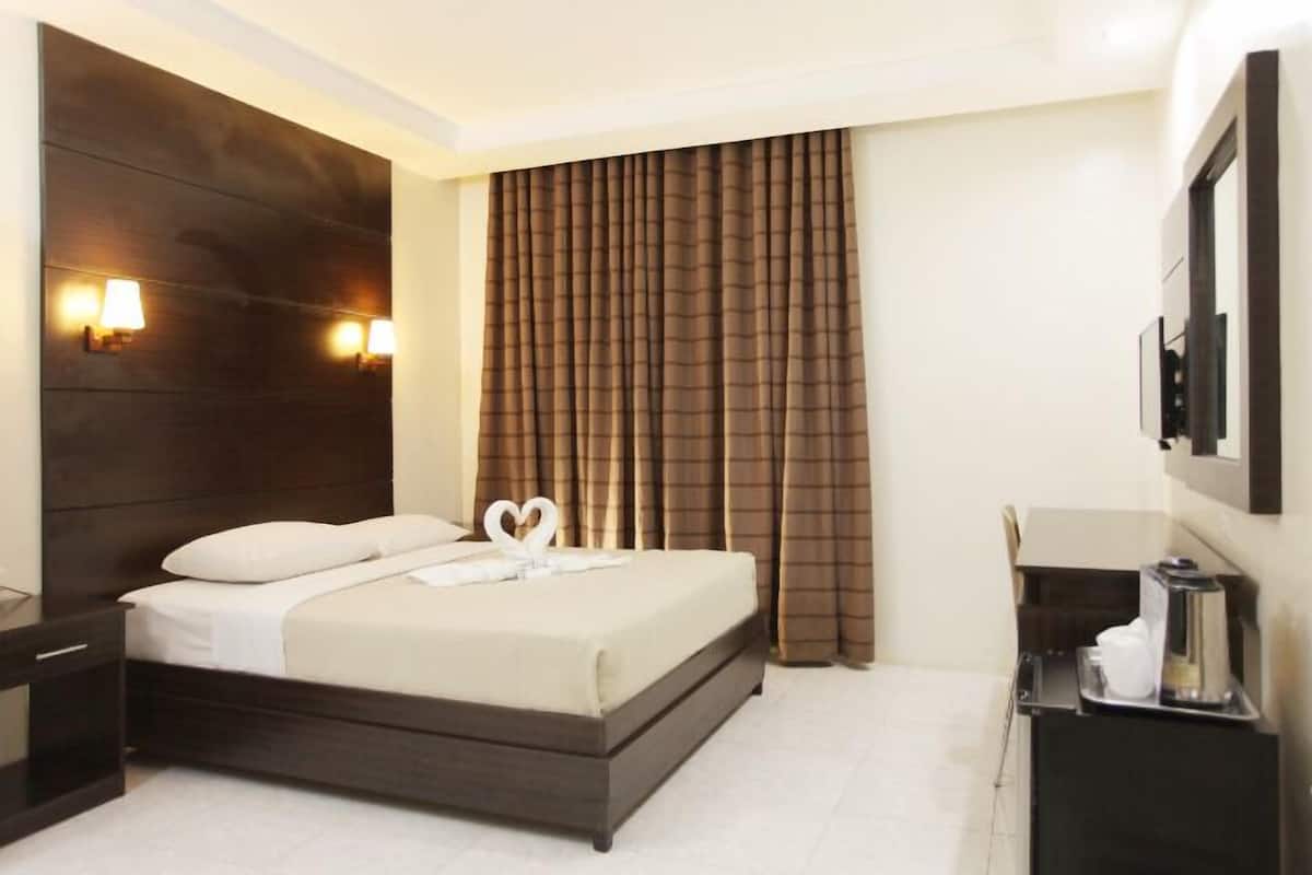 Een hotelkamer met een bed, nachtkastjes, een koffiezetapparaat en een spiegel.