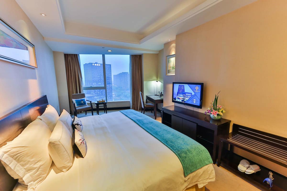 Habitación de hotel con una cama grande, un escritorio con computadora, televisión y vista a la ciudad.