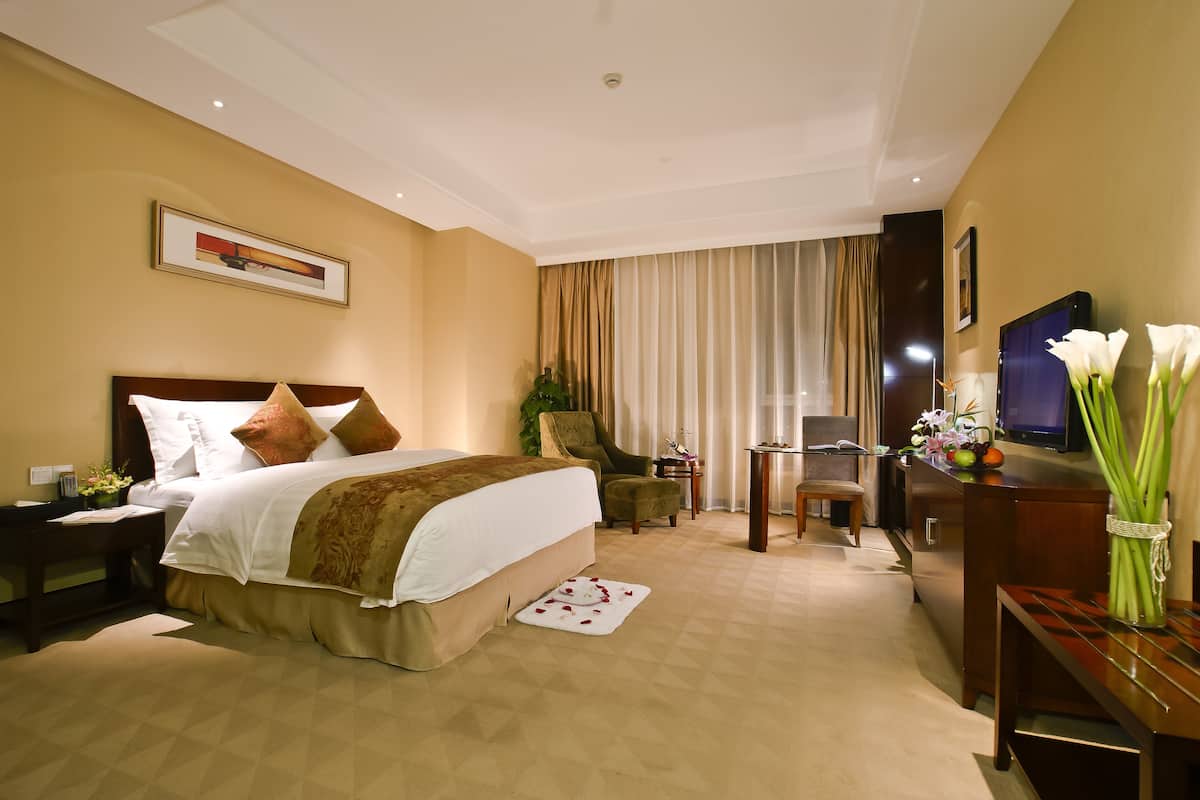 Habitación de hotel con una cama grande, un escritorio, una silla, un televisor y un florero con flores.