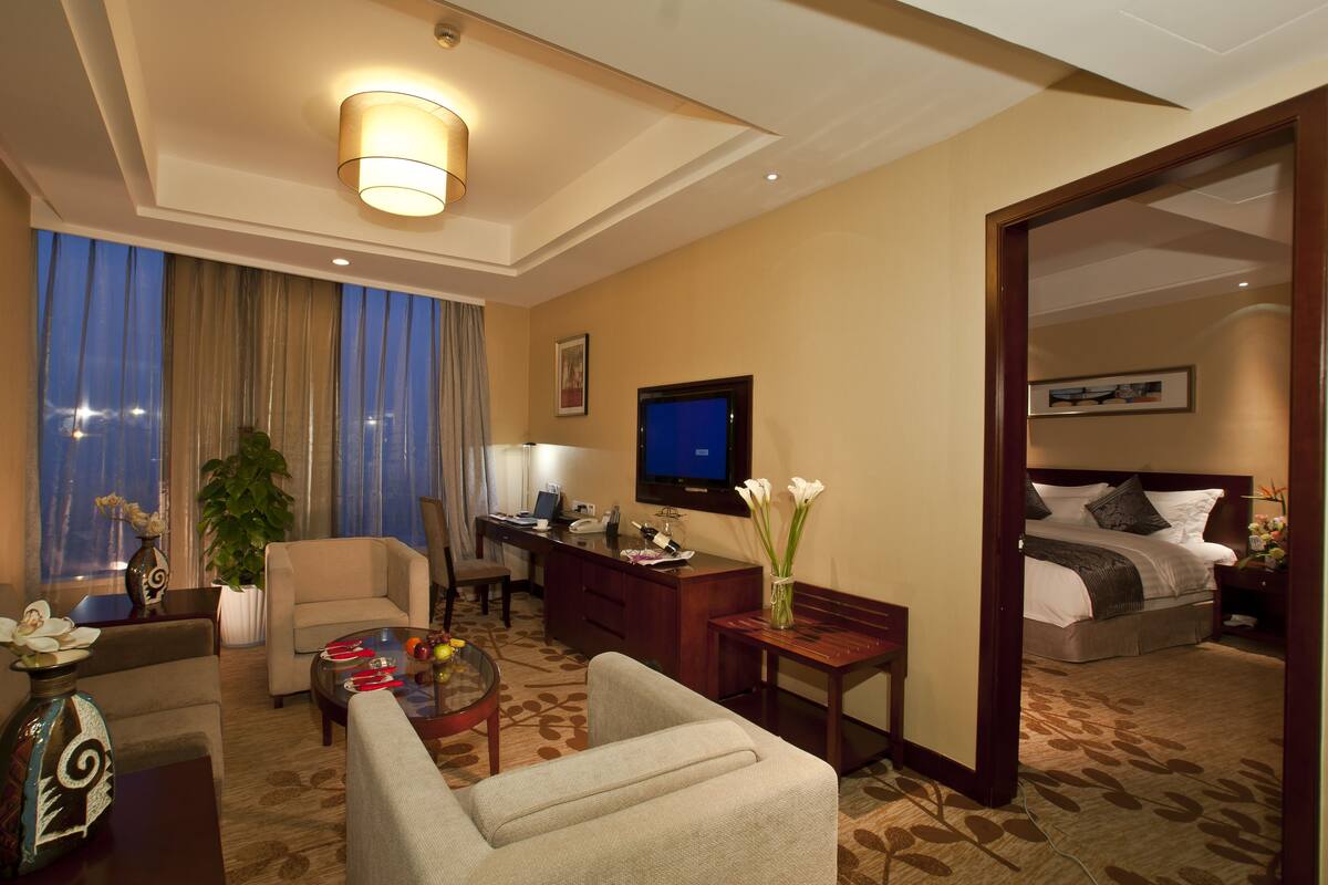 Una habitación de hotel con una cama, un escritorio, un televisor, un sofá, una mesita de centro y una planta en maceta.