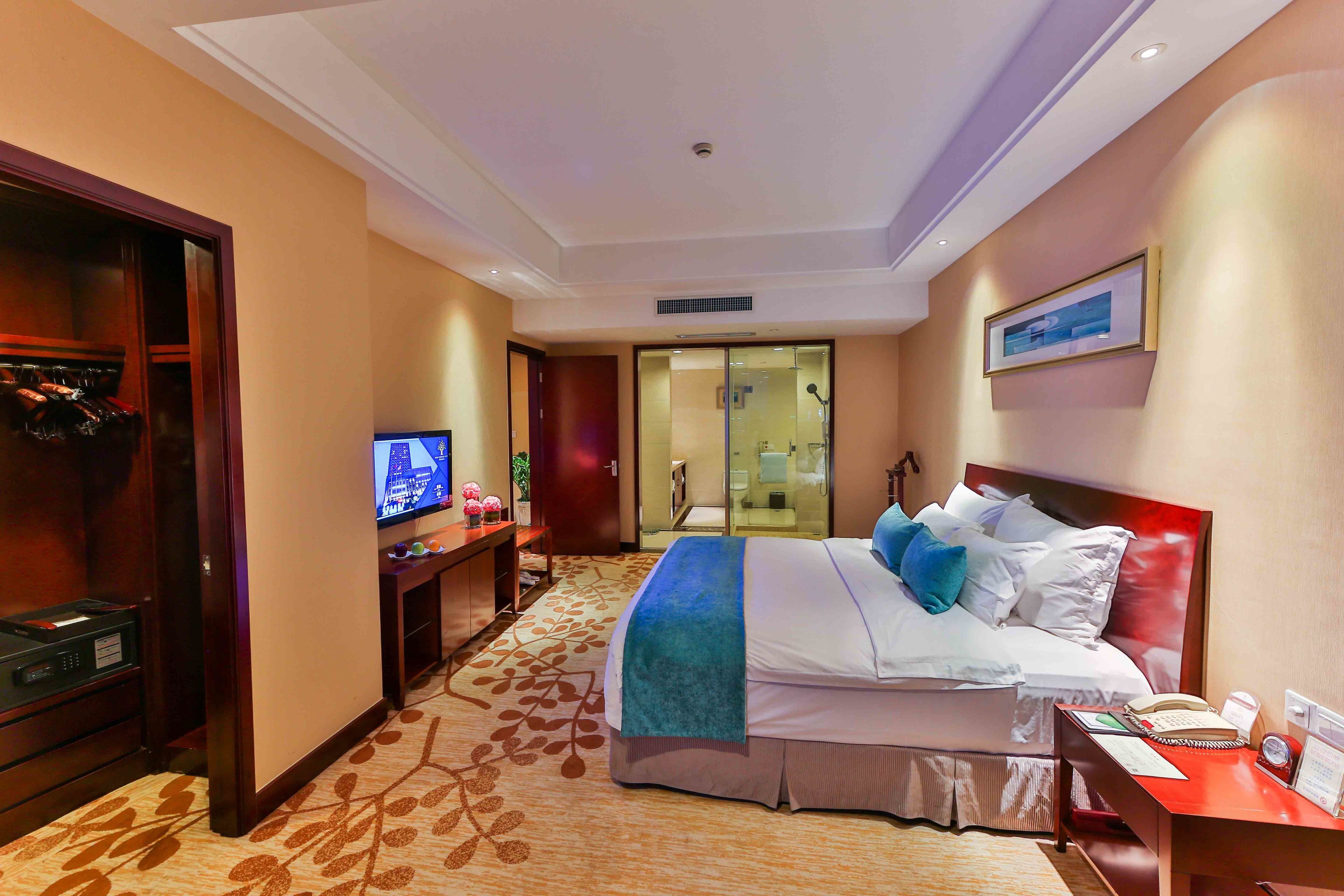 Ein Hotelzimmer mit Bett, Schreibtisch, Fernseher und einem durch eine Glastür einsehbaren Badezimmer.
